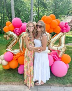 two women standing next to each other in front of balloons