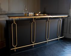 a black and gold bar in the middle of a room with wood flooring, gray walls and cabinets