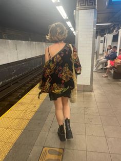 a woman walking down a subway platform with her back turned to the camera and people sitting on benches in the background