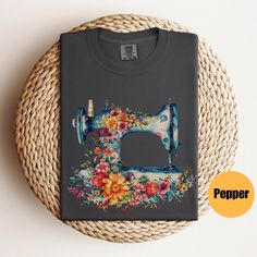 a gray t - shirt with a sewing machine on it and flowers around the front