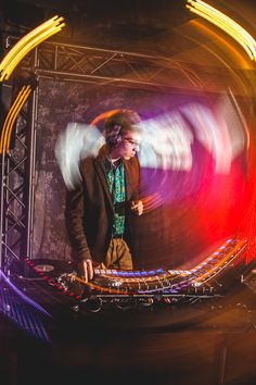 a man standing in front of a dj set with headphones on and lights behind him