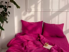 a bed with pink sheets and pillows next to a potted plant