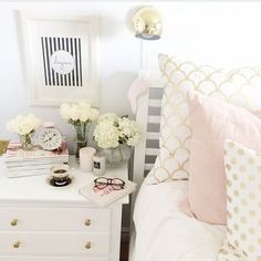 a white bed topped with lots of pillows next to a nightstand filled with books and flowers