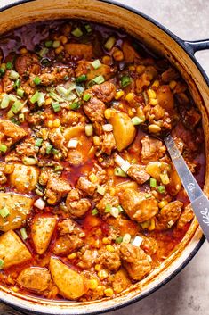 a pot filled with meat and vegetables sitting on top of a counter next to a spoon