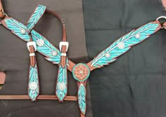 a brown and blue horse bridle with feathers on the side, sitting on top of a black blanket