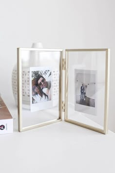 an open photo frame sitting on top of a white table next to a box with two photos in it