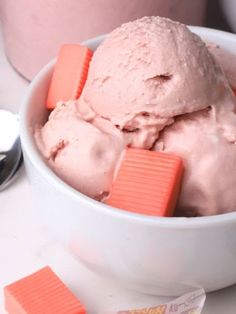 a bowl filled with pink ice cream next to two spoons and a container full of candy