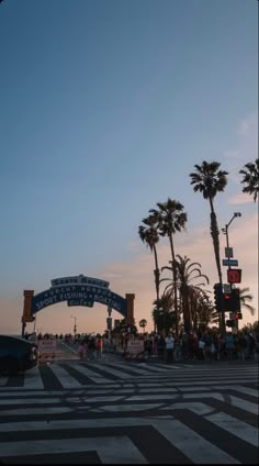 the entrance to an amusement park with palm trees in the foreground and people walking on the sidewalk