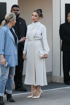 a woman in white coat and heels standing next to other people