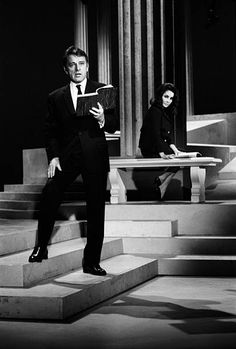 a man in a suit and tie standing on some steps next to a woman holding a tablet