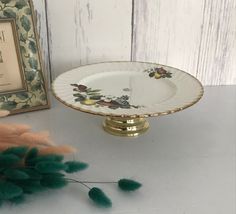 a white and gold plate sitting on top of a table next to a green plant