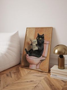 a black cat sitting on top of a toilet reading a book next to a lamp