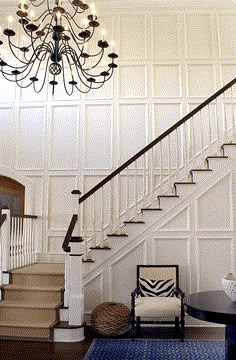 a living room with a chandelier, chair and table in front of the stairs