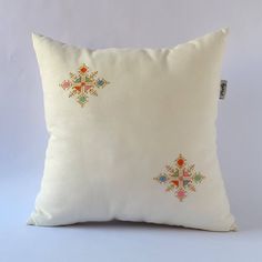 a white pillow with an embroidered cross design on the front and back, sitting against a gray background