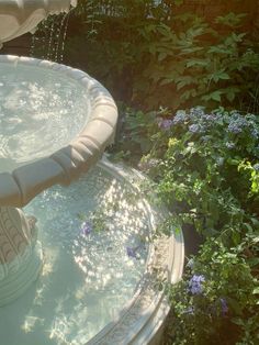 a water fountain in the middle of a garden with flowers growing around it and greenery