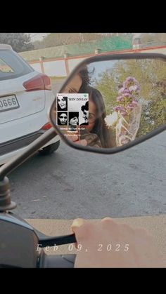 a side view mirror reflecting a woman's face and flowers in the rear view mirror