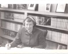 an old black and white photo of a woman sitting at a desk in front of bookshelves