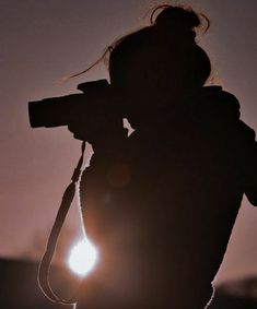 a person holding a camera in front of the sun at sunset or dawn with their back turned to the camera