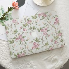 an open laptop computer sitting on top of a table next to a flowery wallpaper