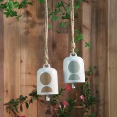 two ceramic bells hanging from twine with flowers in front of wooden fence behind them