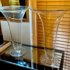 two clear vases sitting on top of a glass table