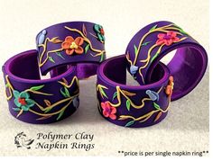 three purple bracelets with flowers painted on them sitting on a white surface next to each other