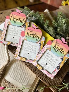 three personalized photo frames sitting on top of an open book next to a pine tree