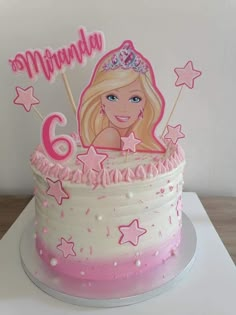 a birthday cake with a barbie doll on top and pink icing, sitting on a table