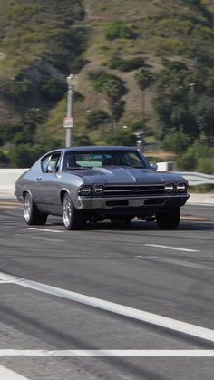 a gray car driving down the road next to a hill