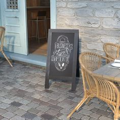 a chalkboard sign sitting on the side of a building next to wicker chairs