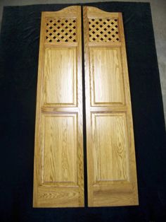 two wooden doors sitting next to each other on a black surface in front of a wall