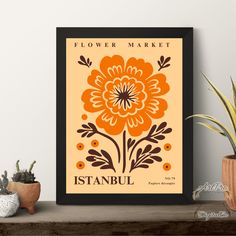 an orange flower market poster hangs on the wall next to a potted plant and succulents