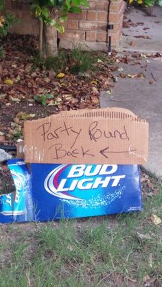 a bud light sign sitting on the ground next to a trash bag and some grass