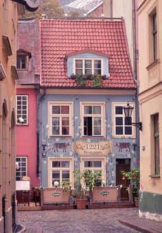 an old building painted blue and pink with flowers in the window boxes on the side