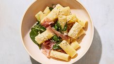 a white bowl filled with pasta and spinach on top of a marble countertop