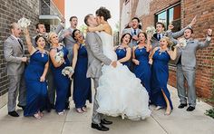 a bride and groom kissing with their wedding party in front of a brick building on the sidewalk