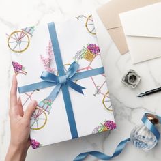 a person holding a wrapped present on top of a white table next to blue ribbon