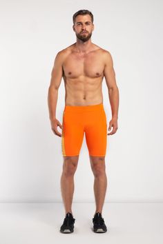 a man with no shirt wearing an orange shorts and black shoes, standing in front of a white background