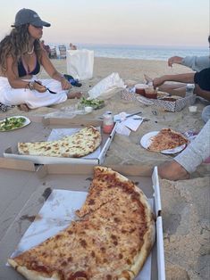 several people sitting on the beach eating pizza