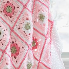 a pink crocheted blanket with white flowers on it and a window in the background