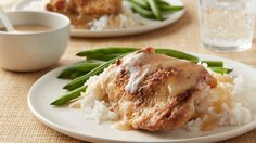 two white plates topped with meat and rice covered in gravy next to a cup of coffee