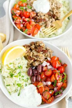 two white bowls filled with different types of food and garnished with lemon wedges