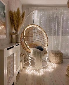 a hanging chair with lights around it in a room that has white curtains and wooden floors