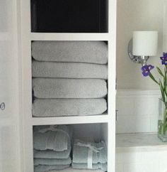 towels are stacked on top of each other in a white cabinet next to a vase with purple flowers