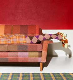 an orange and brown plaid couch sitting in front of a red wall next to a rug