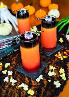 two glasses filled with orange liquid sitting on top of a table next to halloween decorations