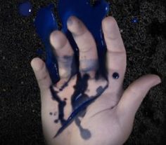 a person's hand with blue paint on it and black ink splatters all over the palm