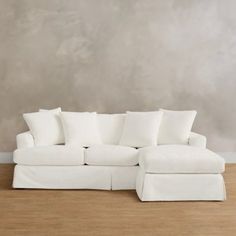 a white sectional couch with pillows on it in front of a gray wall and wooden floor