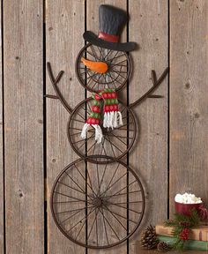 a metal snowman with a top hat and scarf on it's head, standing next to a wooden fence