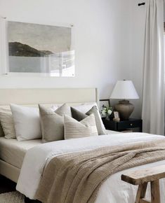 a bed with white linens and pillows in a bedroom next to a painting on the wall